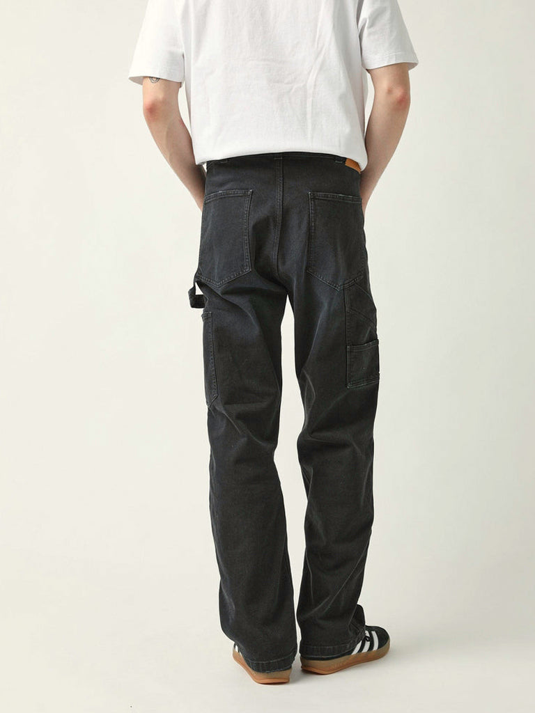 Rear view of a person wearing loose black cargo-style pants with a white T-shirt and black-and-white sneakers, standing against a plain light gray studio background.