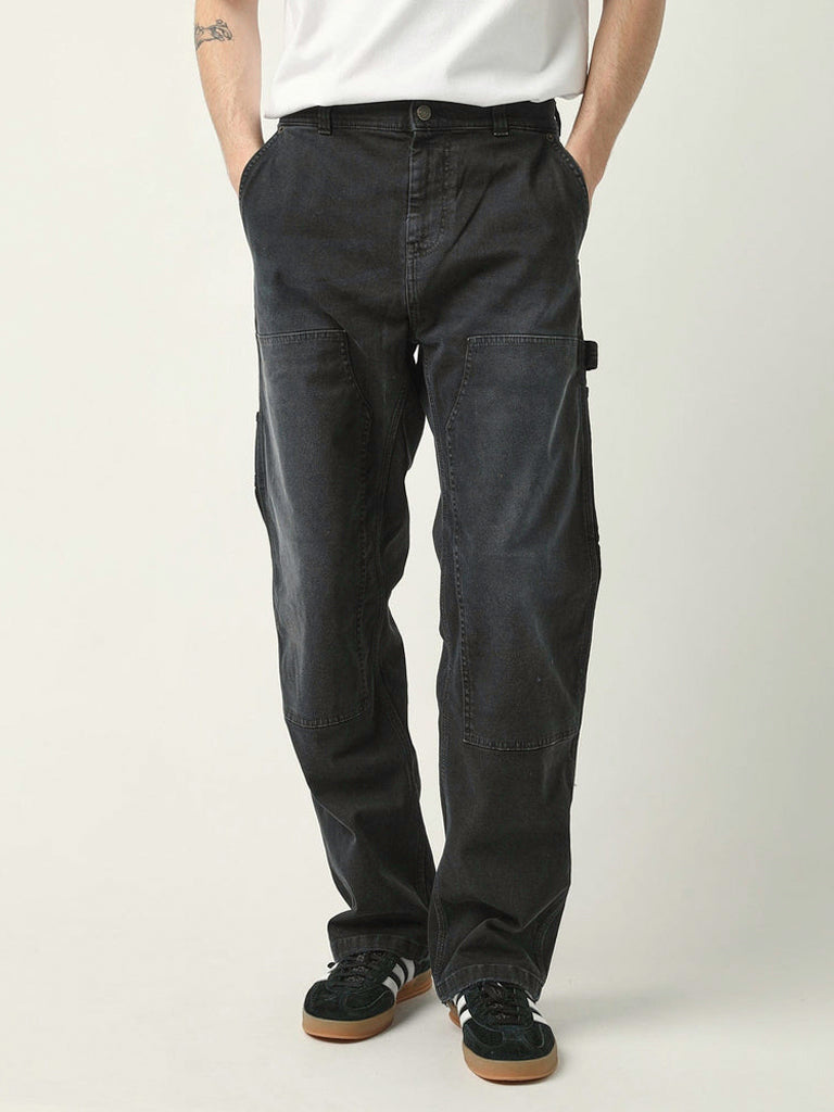 A person wearing black cargo-style pants with a white t-shirt and black sneakers, standing against a light gray studio background.