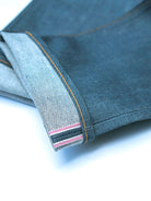 Close-up of folded dark gray denim fabric showing the inner hem with contrast stitching and striped inner lining on a white background.