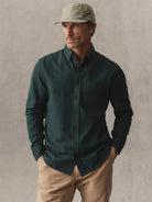 A man wearing a green button-down shirt, khaki pants, and an olive green cap